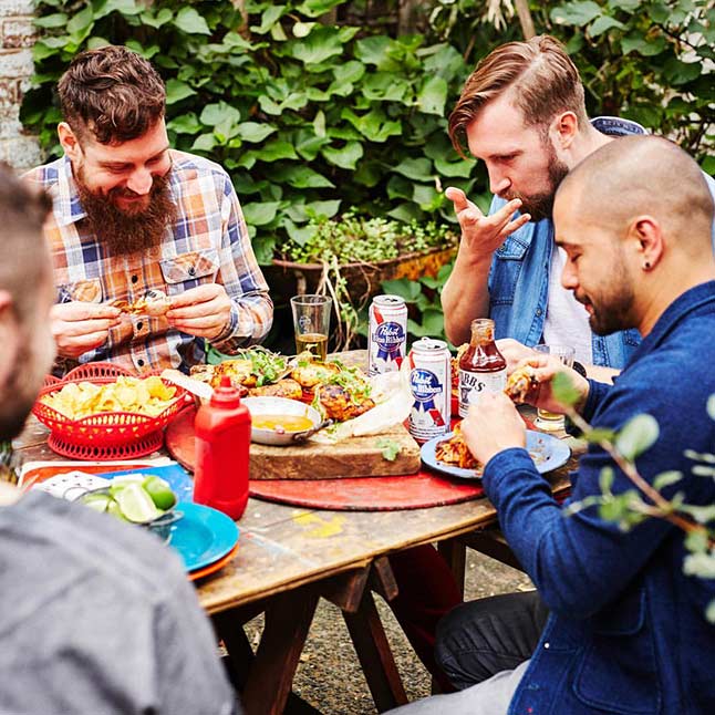 four men sharing a meal outdoor with beer